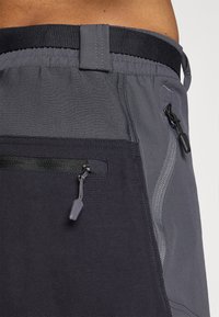 Shorts gris avec une taille texturée, dotés d'une poche zippée et d'un cordon de serrage. Les matériaux présentent un mélange de textures lisses et tissées.