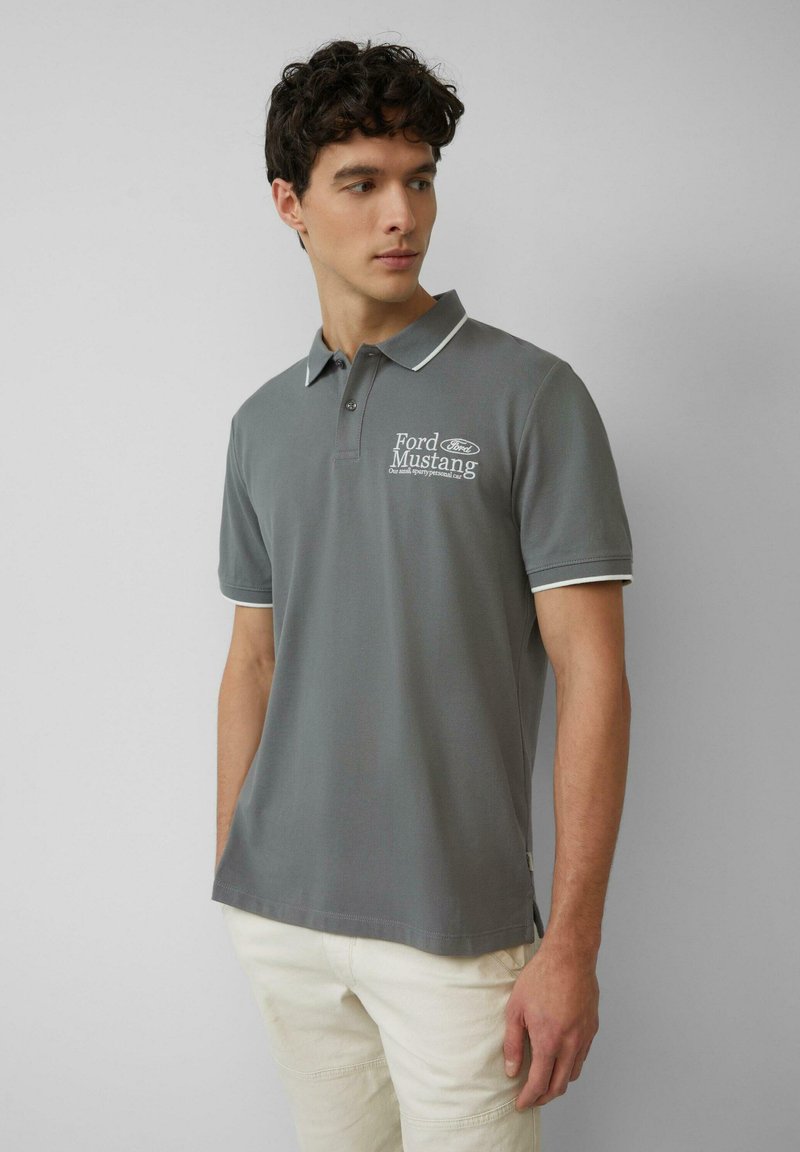 Grijze poloshirt met witte kraag en manchetten, voorzien van een Ford Mustang-logo. Gemaakt van een gladde stof, met een ontspannen pasvorm en zijsplitten.