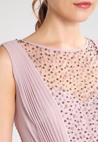 Abito senza maniche in tessuto plissettato lilla con un corpetto trasparente decorato con perline di diverse dimensioni in rosa e argento.