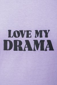Lavender t-shirt made of cotton with a crew neck; features bold black embroidered text reading "LOVE MY DRAMA." Soft texture.