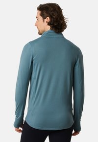 Teal pitkähihaiseen paitoihin, joissa on korkea kaulus ja teksturoitu kangas. Ominaisuuksiin kuuluvat litteät saumat ja peukalonreiät hihojen suissa, slim fit -malli.