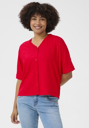 Red short-sleeve shirt with a ruffled V-neck and button front, made from soft fabric, paired with light blue jeans.
