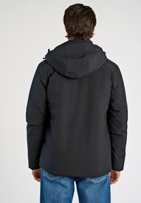 Svart isolerad jacka med huva, med slät tyg, en strömlinjeformad design och utan synlig hårdvara. Bärs över blå denimjeans.