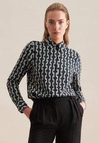 Camicia a maniche lunghe con motivo, caratterizzata da uno sfondo blu navy con catene bianche, e colletto classico. Abbinata a pantaloni neri.
