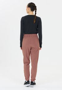 Schwarzes Langarmoberteil mit lockerem Schnitt. Rosafarbene Jogginghose mit elastischem Bund und Bündchen. Schwarze Sportschuhe runden das Outfit ab.