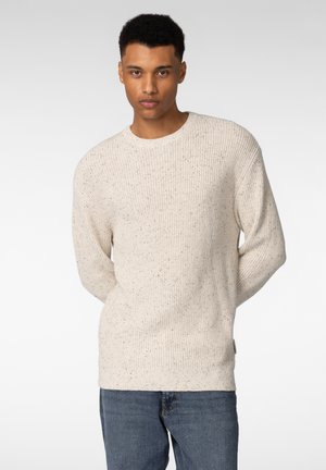 Beige strikkegenser med et strukturert mønster, med rund hals og lange ermer, parret med blå jeans.
