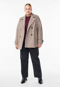 Beige wool blend double-breasted coat with large buttons, notched collar, and side pockets, worn over a dark sweater and black pants.
