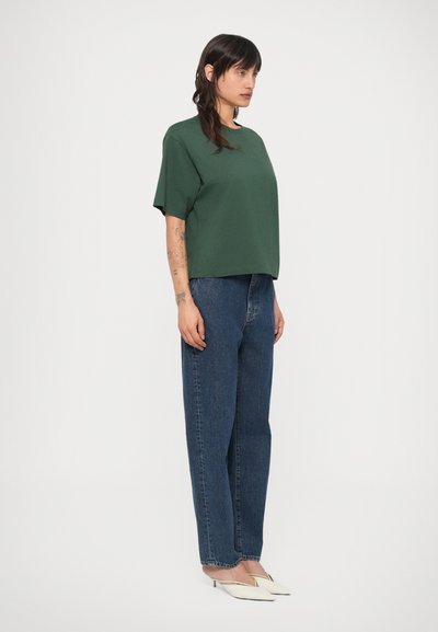 Πράσινο κοντομάνικο μπλουζάκι συνδυασμένο με ψηλόμεσα, μπλε τζιν παντελόνια ίσιας γραμμής. Το σύνολο ολοκληρώνεται με λευκές γόβες μυτερές.