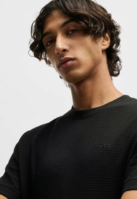 Zwart gestructureerd T-shirt met korte mouwen, voorzien van een ribbelpatroon en een geborduurde "HUGO" logo op de borst.