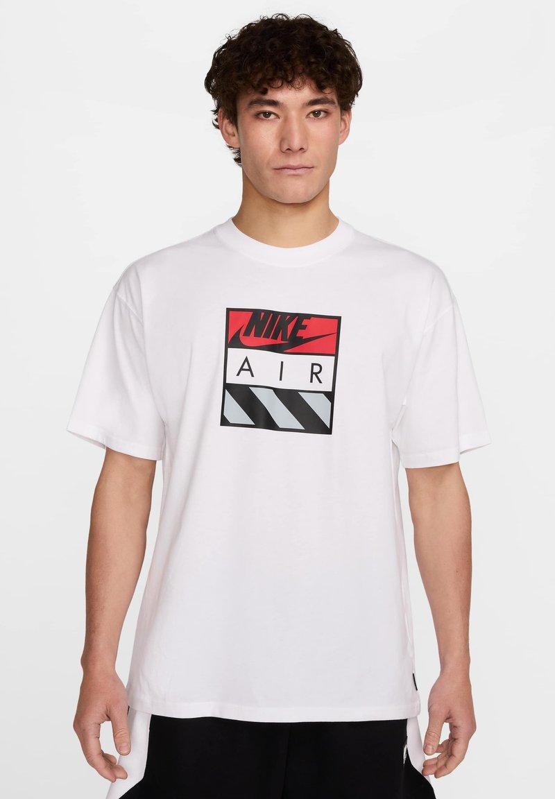 Bela majica s kratkimi rokavi z osrednjim rdečim in črnim logotipom Nike Air na pravokotnem grafičnem dizajnu z diagonálnimi črnimi in sivočrnimi črtami.