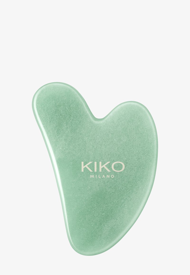 Grønn jade gua sha-stein med "KIKO MILANO"-logoen trykt i hvitt på en enkel lys bakgrunn.