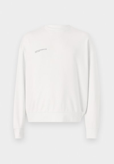 Biely sveter s dlhými rukávmi, klasickým výstrihom a rebrovaným lemom. Obsahuje minimálny textový detail na hornej ľavej strane. Vyrobený z mäkkej zmesi bavlny.