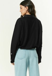 Sort langærmet skjorte med krave, afslappet pasform og knaplukkede manchetter. Sammen med lyseblå brede bukser. Minimalistisk detaljeret.
