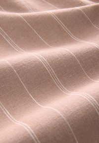 Pink stof med en tekstureret overflade, der har tynde hvide striber. Stofet virker blødt med subtile bølger og folder.