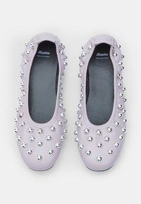 Bailarinas de cuero de color lila claro adornadas con tachuelas de metal plateado, con punta redonda y una plantilla suave y acolchada. Plantillas negras con el logo de la marca visible.