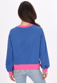 Felpa blu con accenti rosa al colletto e all'orlo, caratterizzata da una vestibilità comoda e maniche a palloncino, realizzata in tessuto morbido.