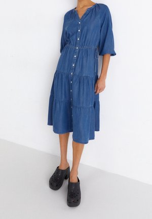 Woman wearing a blue button-down midi dress with three-quarter sleeves and black platform clogs with ventilation holes.