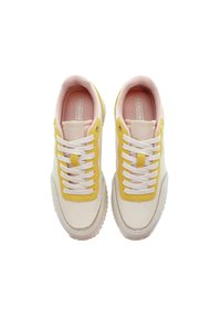 Sneakers med vit bas, gula mockadetaljer och rosa tygfoder. Funktioner inkluderar vita snören, rund tå och texturerad gummisula.