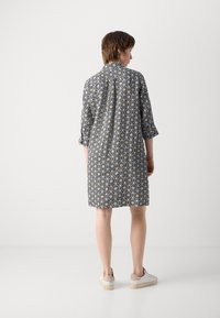 Abito camicia a maniche corte con motivo in bianco e nero, colletto e vestibilità ampia. Indossato con scarpe con plateau di colore chiaro.