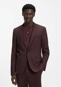 Bordeauxrotes Sakko mit Spitzrevers, zwei Vorder Taschen und schwarzen Knopfdetails, getragen über einem passenden bordeauxroten Hemd mit Logo.