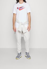 White T-shirt with multicolored Nike logo, light gray joggers, and gray athletic shoes with yellow accents. T-shirt tied around waist.