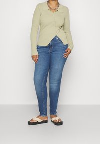 Cárdigan de color verde claro con canalé, con cuello, botones en la parte delantera y dobladillo en ángulo. Combinado con jeans skinny azules y sandalias de tiras color crema con suela negra.