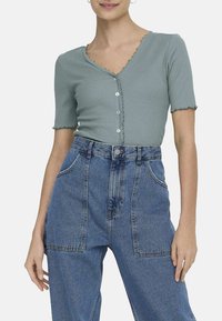 Haut à manches courtes en vert doux avec un col festonné et une fermeture à cinq boutons, associé à un jean wide-leg en denim bleu taille haute.