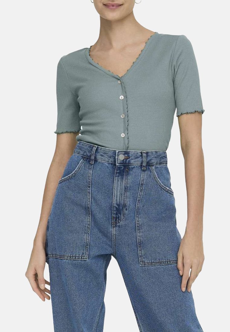 Haut à manches courtes en vert doux avec un col festonné et une fermeture à cinq boutons, associé à un jean wide-leg en denim bleu taille haute.