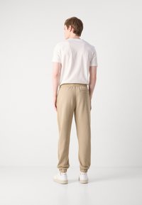 Beige joggebukser med elastiske mansjetter og midjebånd, med en baklomme og subtile sømdetaljer. Kombinert med en enkel hvit t-skjorte.