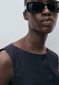 Navy pinstriped dress with a round neckline and a side button detail, paired with oversized black sunglasses. Smooth fabric and minimalist design.