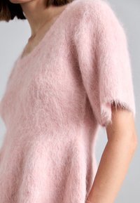 Světle růžový chlupatý pletený svetr s širokým výstřihem a krátkými rukávy. Měkká textura s uvolněným střihem a jemným leskem.