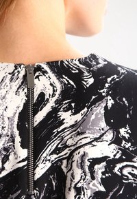 Černobílé šaty s mramorovým vzorem, se zapínáním na zip na zádech a hladkým materiálem. Design má kulatý výstřih.