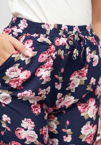 Blomstrede joggebukser i marineblått stoff, med rosa og kremfargede blomster. Elastisk midjebånd med snøring og sidelommer. Glatt tekstur.