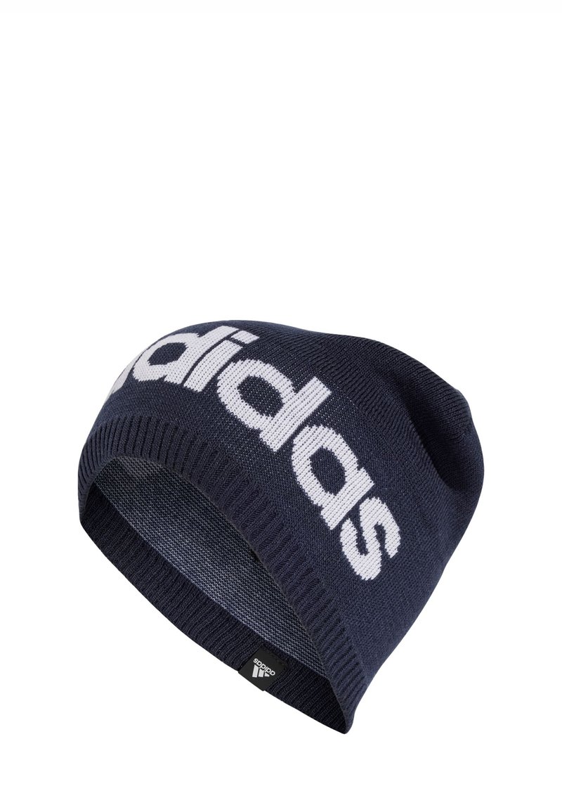 Navy knit beanie with a white "adidas" logo. Features a ribbed cuff and smooth texture. Includes a small black brand tag at the hem.