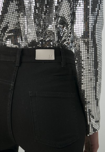 Jeans noirs taille haute en tissu texturé avec poches arrière, agrémentés d'une étiquette rectangulaire en métal argenté sur laquelle est embossé un "M".