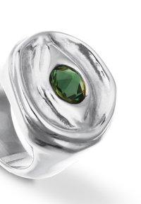 Anillo de plata con un diseño suave y escultórico, que presenta una piedra preciosa verde facetada en el centro, reflejando la luz con un acabado pulido.