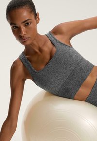 Sutien sport și colanți dintr-un material texturat, gri, cu decolteu pătrat și bretele late. Modelul pozează pe o minge de exerciții de culoare deschisă.