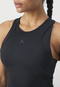 Top sin mangas atlético negro con una textura suave, que presenta un diseño curvado y un logo Jumpman gris en el centro.