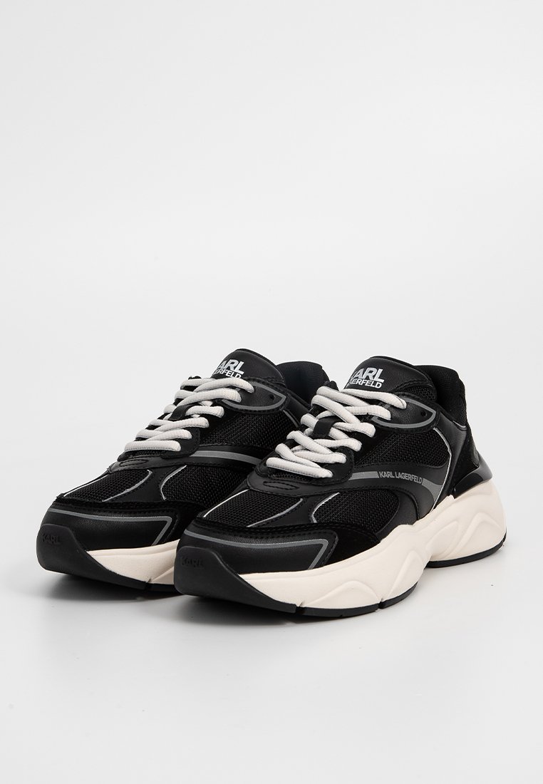 Baskets noires avec une tige en maille et en daim, présentant des accents gris clair, un bout arrondi, une épaisse semelle intermédiaire blanche et des lacets contrastants.