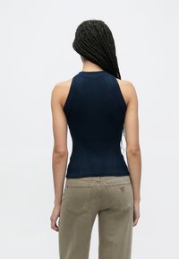 Top azul-marinho de malha canelada sem mangas com design estruturado e gola alta, combinado com jeans verde-oliva claro.