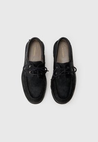 Zwarte moccasin-stijl schoenen met een getextureerde, vachtachtige bovenkant, leren accenten, gouden ogen en platte veters. Contrasterende stiksels langs de randen.