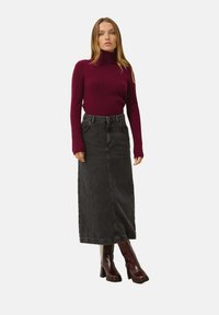 Burgundin värinen ribbitetty turtleneck-neule yhdistettynä korkeavyötäröiseen mustaan farkkukmaxiin. Mallilla on yllä kiiltävät burgundin väriset nilkkurit.