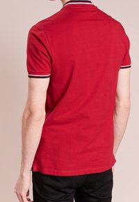 Röd polo t-shirt med klassisk passform, har korta ärmar och en svart-vit randig krage. Materialet verkar slätt och bomullslikt.