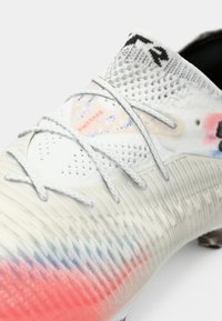 Football boot with a white upper, gradient pink and blue pattern, textured design, and grey laces. Features prominent branding and perforations.