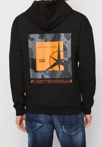 Černá mikina s kapucí vyrobená z bavlny, se zdobným velkým barevným grafickým potiskem s oranžovými akcenty a textem na zadní straně. Kanga kapsa vpředu.