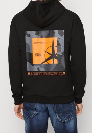 Musta huppari, joka on valmistettu puuvillasta, ja jossa on suuri värikäs graafinen kuvitus oransseilla yksityiskohdilla ja tekstiä selässä. Edessä kengurupocket.
