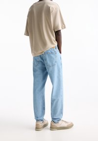 Camisa beige de manga corta, vaqueros de mezclilla azul claro y zapatillas beige; ajuste relajado con bolsillos traseros y detalles de costura sutiles.