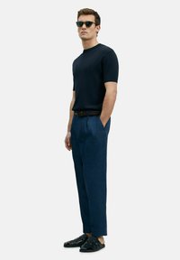 Marineblauw geribbelde top met korte mouwen, zwarte op maat gemaakte broek en zwarte sandaaltjes met bandjes. Zonnebril completeert de algehele outfit.