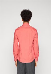 Long-sleeve shirt in coral, tailored fit, cotton blend fabric, featuring a standard collar and buttoned cuffs, smooth texture, minimal detailing.