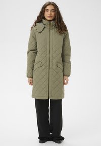 Abrigo largo acolchado de color verde oliva con cuello alto, cierre de cremallera y dos bolsillos delanteros. Textura lisa con patrón geométrico de costuras.